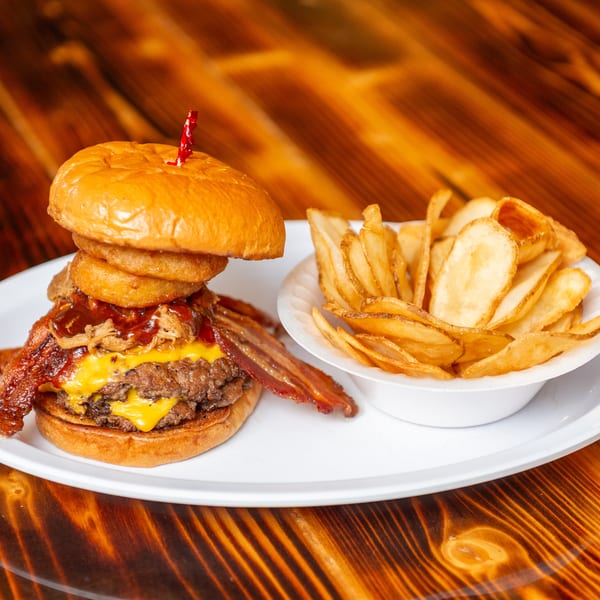 A towering burger with bacon, pulled pork, onion rings, and cheese, served with potato chips.