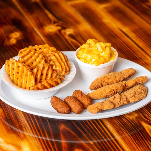 A plate of fried chicken tenders, waffle fries, mac and cheese, and hush puppies on a wooden table.