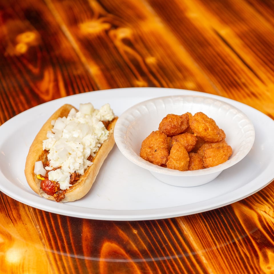 Chili dog with mustard, onions, and coleslaw, served with a side of fried hushpuppies.