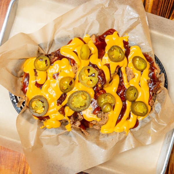 Pulled pork nachos with melted cheese, barbecue sauce, and sliced jalapeños on parchment paper.